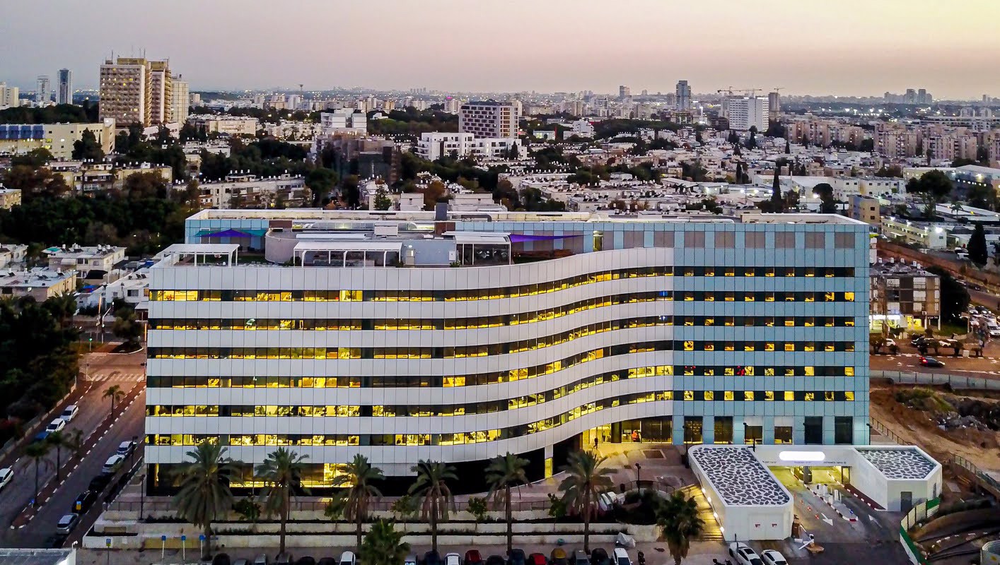 קמפוס אמות בגבעתיים: בניין המשרדים הראשון בישראל בטכנולוגית אנרגיה ירוקה אמות השקעות גאה להוביל את מהפכת הבנייה הירוקה בישראל עם קמפוס אמות בגבעתיים, שהפך לבניין המשרדים הראשון בארץ המוגדר כבניין מאופס אנרגיה ומאופס פחמן. בצעד משמעותי לקידום תפיסת הקיימות במרחב הבנוי, קמפוס אמות בגבעתיים מהווה דוגמה חדשנית לאופן שבו נדל"ן מניב יכול לתרום לא רק לתשואה כלכלית, אלא גם לתועלת סביבתית רחבה. השילוב בין תכנון אדריכלי חכם, מערכות טכנולוגיות מתקדמות וסטנדרטים גבוהים של יעילות אנרגטית הפך את הקמפוס לאב-טיפוס לבנייני העתיד במרחב האורבני הישראלי.  שילוב מתקדם של אסתטיקה, קיימות ויעילות אנרגטית מערכת הפאנלים הפוטו-וולטאיים שהותקנה בחזיתות המבנה, בשיתוף עם קבוצת אלומיניום קונסטרקשיין, נועדה להפיק אנרגיה סולארית גם מקירות המבנה ולא רק מהגג, כפי שהיה נהוג בעבר. הטכנולוגיה החדשנית מאפשרת שילוב של תאים סולאריים בתוך זכוכית צבעונית שקופה חלקית, המשלבת אסתטיקה עם תפקוד פונקציונלי ברמה הגבוהה ביותר. בכך הופכות החזיתות למשטח יצרני, שמייצר חשמל בצורה שקטה, נקייה ואפקטיבית. המערכת פועלת באמצעות טכנולוגיה של חברת SolarEdge, הנחשבת לאחת המובילות בעולם בתחום האופטימיזציה של מערכות סולאריות. פתרון זה מספק יעילות אנרגטית גבוהה במיוחד, ומבטיח שימוש מרבי באנרגיה המתחדשת, תוך מזעור הפסדים. חזון תכנוני בר קיימא טל אהרון, מנכ"ל סמארטקון מקבוצת אלומיניום קונסטרקשיין, מדגיש את ההיבט החזוני של הפרויקט:  "אנחנו רואים בקמפוס הזה התחלה של עידן חדש. המעבר לניצול אנרגטי חכם של החזיתות הוא לא רק פתרון סביבתי – אלא גם צעד טבעי לשילוב טכנולוגיה מתקדמת בבנייה אדריכלית מודרנית. המפעל החדש שאנו מקימים בישראל לייצור פאנלים אדריכליים יוביל את התחום קדימה, ויאפשר להנגיש פתרונות אנרגיה חכמים לפרויקטים נוספים ברחבי הארץ."  סביבת עבודה מתקדמת ובריאה עופר בן צור, סמנכ"ל השיווק באמות השקעות, מציין כי הקמפוס פותח מתוך מחויבות לערכים של קיימות, חדשנות ורווחת העובדים:  "יצרנו סביבת עבודה שתומכת בבריאות, ביצירתיות ובפרודוקטיביות של המשתמשים. אור טבעי, תחלופה גבוהה של אוויר, נגישות לתחבורה ירוקה ומתקני רווחה מתקדמים. כל אלו הם חלק בלתי נפרד מהחזון שלנו בנוגע לעתיד העבודה במרחב האורבני." נתונים ומאפיינים עיקריים של הקמפוס: קמפוס אמות בגבעתיים מציע סביבת עבודה מתקדמת ומודרנית, המשתרעת על פני שטח של כ-17,500 מ"ר של משרדים להשכרה, אשר שווקו במלואם לחברות מובילות במשק. בין שוכרי העוגן הבולטים ניתן למנות את חברת SimilarWeb, ששוכרת חמש קומות בקמפוס, ואת חברת NextSilicon, המחזיקה בשתי קומות נוספות. קומת הקרקע של הבניין מרווחת במיוחד, וכוללת מגוון חללים לשימוש יומיומי ועסקי כגון אולמות כנסים, אודיטוריום, חדרי כושר, מתחמי יוגה ומטבחי שף מאובזרים. על גג הבניין תוכננו מתחמי rooftop לפנאי, ישיבות ואירועים לעובדים. הקמפוס כולל חניון תת-קרקעי המכיל כ-450 מקומות חניה, וממוקם בצמוד לצומת השלום, מה שמבטיח נגישות מצוינת לרכב פרטי, תחבורה ציבורית ואף הגעה נוחה באמצעות אופניים וקורקינטים.   דירוגים סביבתיים מרשימים לאחר השקעה כוללת של כ-100 מיליון ש"ח בתכנון, פיתוח והתאמה לתקנים מתקדמים, מציב קמפוס אמות בגבעתיים רף חדש באיכות התשתיות ובביצועים האנרגטיים של מבני משרדים בישראל. הקמפוס נהנה ממערכת מיזוג אוויר חכמה ויעילה במיוחד, המתוכננת להעניק חוויית שימוש מיטבית תוך צריכת אנרגיה מופחתת משמעותית. נוסף לכך, מעטפת המבנה חופתה בפאנלים פוטו-וולטאיים מתקדמים המשלבים יכולת לבידוד תרמי ברמה גבוהה עם ייצור עצמי של חשמל סולארי, מה שתורם הן לחיסכון תפעולי והן להפחתת טביעת הרגל הפחמנית של המבנה. כל אלה יחדיו הובילו את הקמפוס לעמידה בתקן הבינלאומי המחמיר LEED Platinum V4, הנחשב לדירוג הגבוה ביותר לבנייה ירוקה בעולם, ומעיד על מחויבות חסרת פשרות לאיכות סביבתית, קיימות ואחריות תכנונית ארוכת טווח.  חיבור בין טכנולוגיה, אדריכלות וסביבה קבוצת אלומיניום קונסטרקשיין, שפועלת למעלה מ-30 שנה, מתמקדת בפיתוח מערכות מעטפת המשלבות בינה מלאכותית, שליטה חכמה וחדשנות אסתטית – מתוך הבנה כי המעטפת האדריכלית משפיעה באופן ישיר על חוויית המשתמש, רווחתו ותפקודו. הקבוצה מחזיקה בלמעלה מ-50 מערכות מעטפת חדשניות, שזכו לשבחים ולהכרה בפרויקטים מובילים בארץ ובעולם. הפאנלים הפוטו-וולטאיים שפותחו על ידי הקבוצה משתלבים בצורה מושלמת עם מערכות אחרות במבנה ותורמים לא רק לחיסכון אנרגטי – אלא גם להפחתה משמעותית של פליטות פחמן, תוך שמירה על עיצוב מוקפד, איכות ופונקציונליות. אמות השקעות ממשיכה להציב סטנדרטים חדשים בתחום הנדל"ן המניב בישראל. קמפוס אמות בגבעתיים הוא לא רק פרויקט פורץ דרך, אלא ביטוי מוחשי למחויבות ארוכת השנים שלנו לשילוב בין חדשנות, קיימות וניהול איכותי של נכסים.